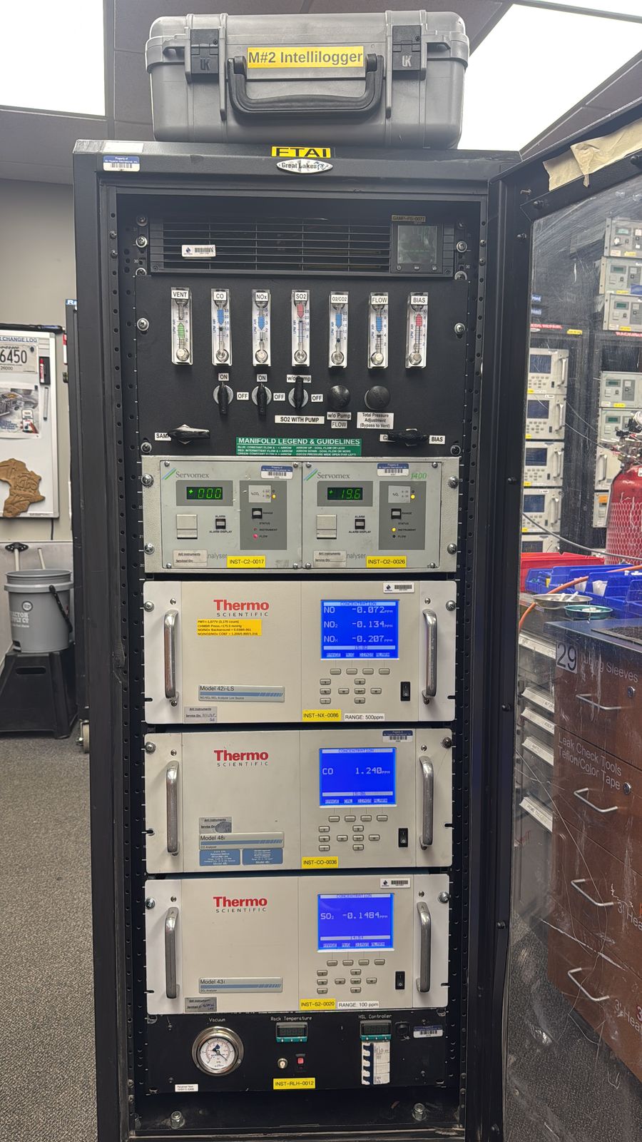 A CEMS rack of analyzers powered up on the warehouse floor, a transit case stowed on top