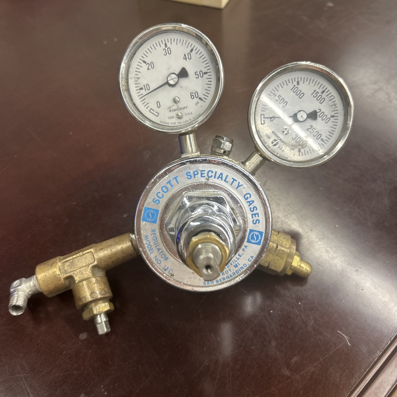 A Scott Specialty Gases model 18C two-stage regulator with a pair of Ashcroft gauges, brass fittings tarnished, on a workbench