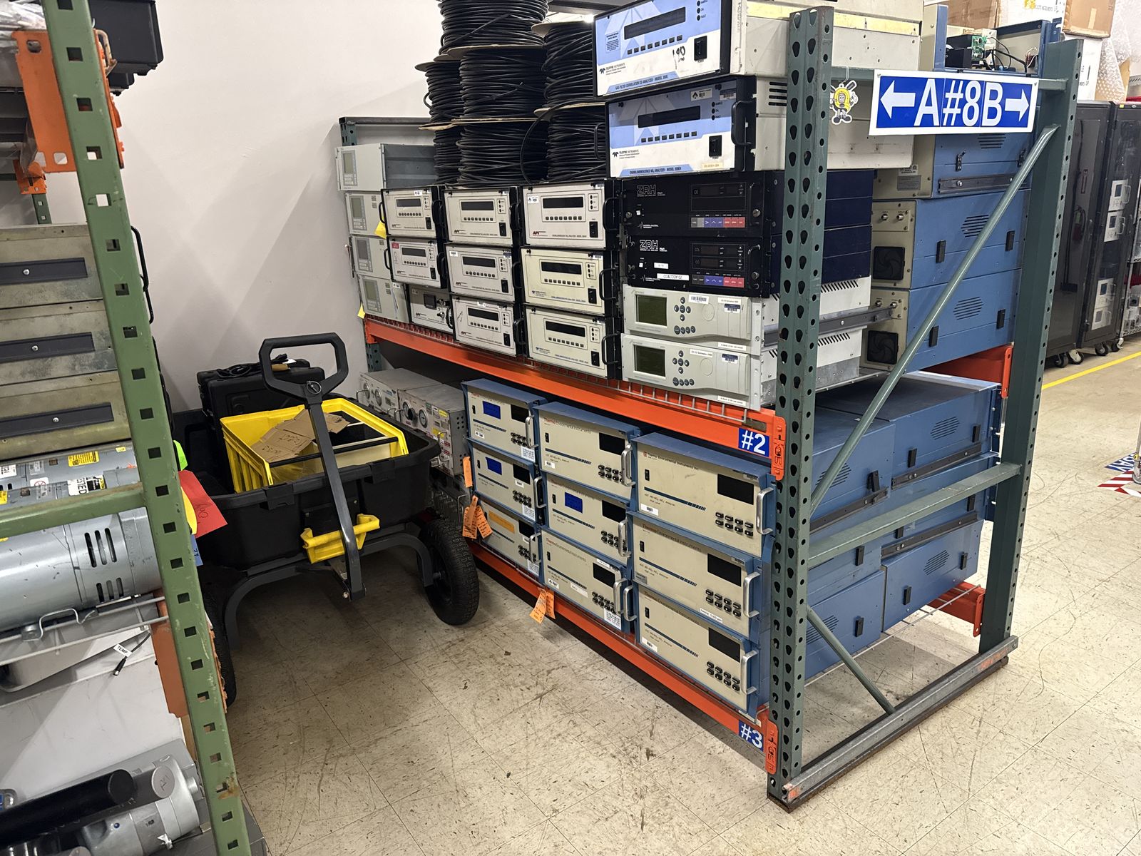 A warehouse aisle of pallet racking stacked with analyzers and instrument cases, a pallet jack parked at the end